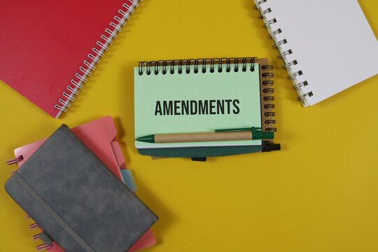a spiral notebook with the word &ldquo;Amendments&rdquo; surrounded by colorful notebooks and a pen on an yellow background, representing legal changes, document revision, policy updates, and business planning.