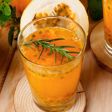 Tropical passion fruit refresher served in a glass vessel, accompanied by rosemary, fresh fruit, and rustic wood.