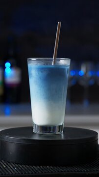 Blue Matcha Iced Latte In Glass With Straw Rotates Against Blurred Bar Lights Background. Vertical Video