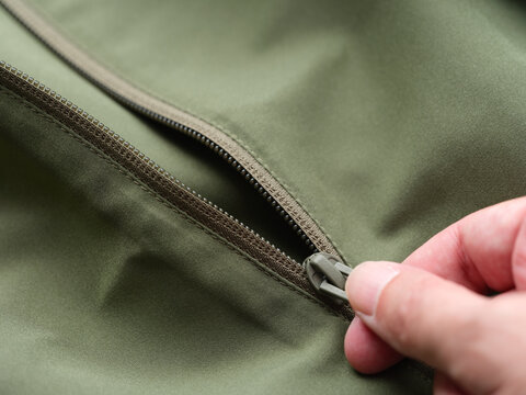 Close-up of a person's hand pulling the zipper slider on a green fabric jacket.