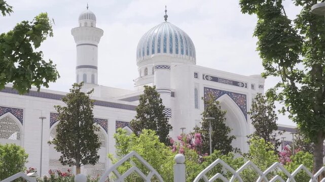 Smooth left-to-right camera movement showing the Grand Mosque in Dushanbe framed by trees and foliage in the foreground