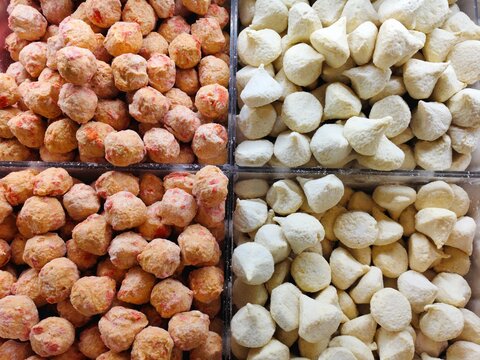 Variety of raw, frozen Asian meatball snacks arranged in clear retail containers.