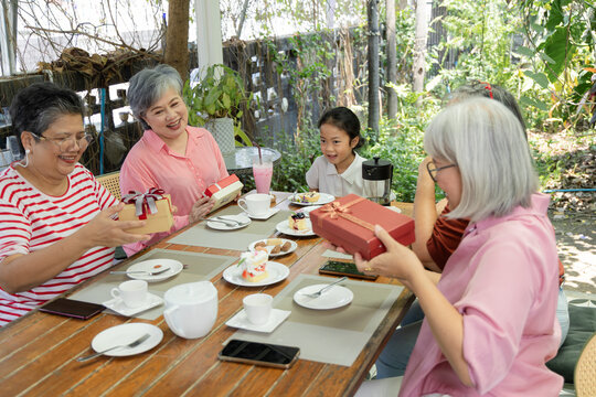 Older friends share tea and cake at an outdoor cafe, smiling with cups in hand during a relaxed reunion full of easy conversation, laughter and warm companionship on a sunny afternoon, aging society.
