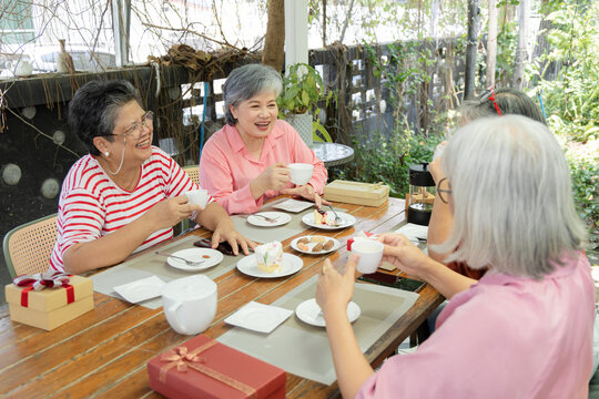 A circle of friends and a young girl gather at an outdoor cafe, sharing tea, cake and conversation around the table during a calm reunion shaped by companionship and family moments, aging society.