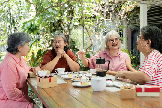 Longtime friends enjoy tea and desserts at an outdoor cafe, chatting across the table during a warm reunion shaped by easy laughter, companionship and shared time together with ease, aging society.