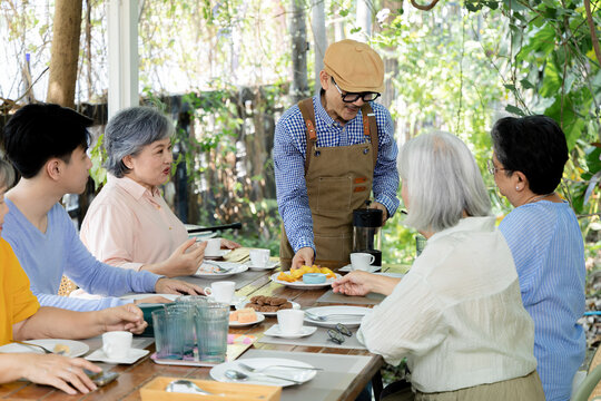 A cafe waiter serves refreshments to senior friends and a young man at an outdoor table, capturing attentive service, shared snacks and the relaxed pleasure of reunion dining together, aging society.