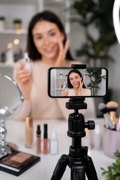 Close up focus on smartphone screen recording a female beauty blogger demonstrating facial serum and cosmetics at her makeup table.