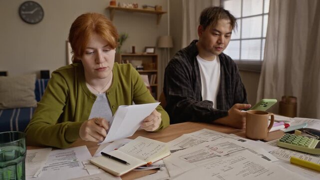 Young adult Caucasian woman and Asian man managing home budget, reviewing past due utility bills at table. Footage perfect for financial planning and debt relief services