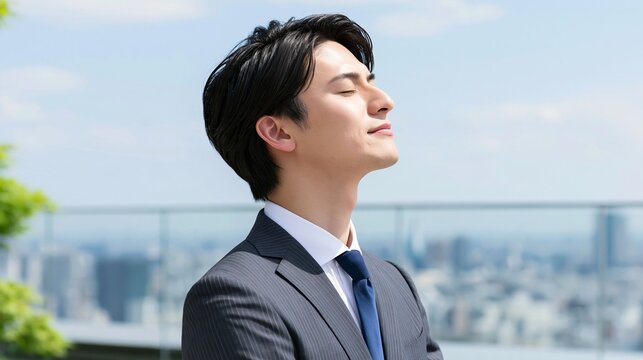 都会の風を感じて目を閉じ爽やかな笑みを浮かべるスーツ姿の若い男性