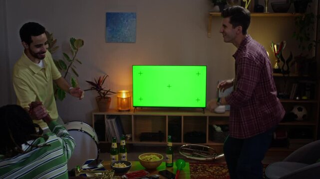 Diverse young adult male sports fans celebrating victory in front of green screen television display, rear view zoom out. Clip ideal for sports app and media campaign mockups