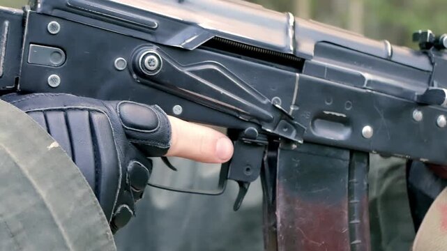 Close-up of a soldier holding an automatic assault rifle with tactical gloves, focusing on the trigger and receiver