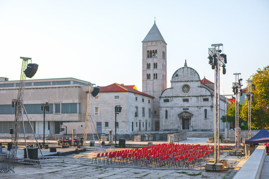 Roman Forum in Zadar, Croatia, historic St. Mary Church and its stone bell tower. Outdoor stage setup with rows of red chairs stands ready for a public performance
