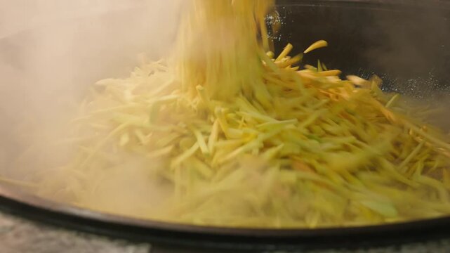 Adding sliced carrots to traditional Uzbek plov. Authentic Central Asian cooking, tourism, travel