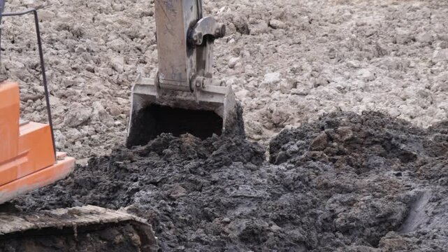 Raw industrial power meets stubborn, saturated soil; thick mud clings to the bucket as the machine wrestles the unyielding terrain