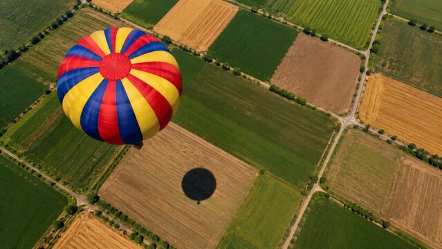 A colorful hot air balloon flying over a patchwork of fields and farmland on a sunny day.