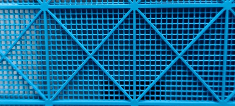 Close‑up of a rigid blue plastic grid featuring small square openings and diagonal beams forming triangular patterns. The geometric design highlights industrial precision and structural durability.