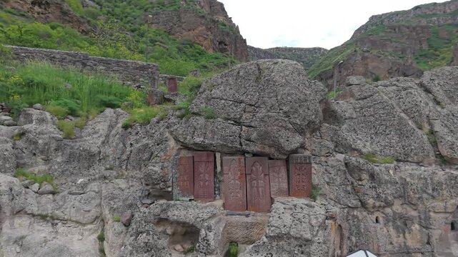  Wall of the ancient monastery made of volcanic stone Geghard, Armenia. Crosses in the rock near monastery of Geghard. Intricately carved stone khatchkars stand on a rocky hillside at Geghard Monaster