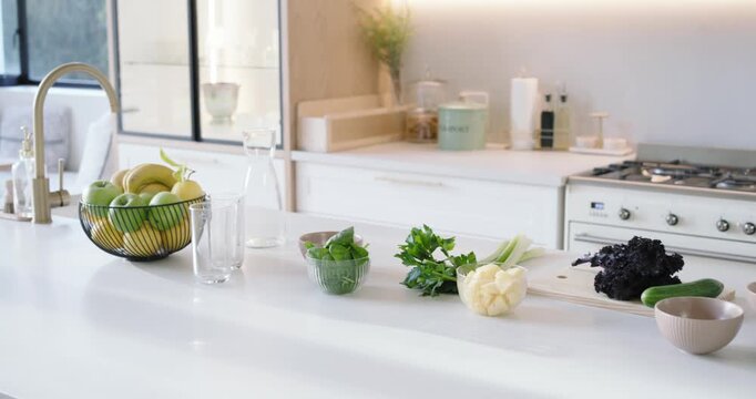 Camera is panning right, revealing counter produce and blender in bright kitchen for smoothie prep