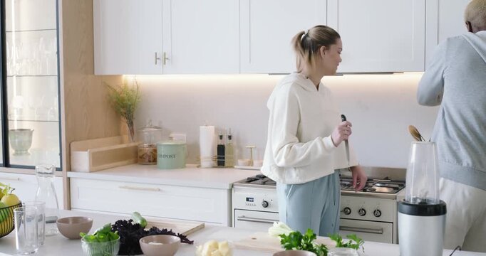 Couple in kitchen woman tasting pot chopping cucumber on board while man chopping celery for dinner