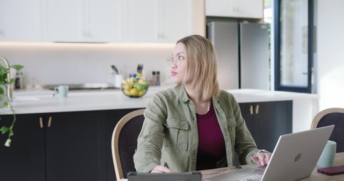 African American woman in jacket adjusting tablet typing on laptop at kitchen table as man entering