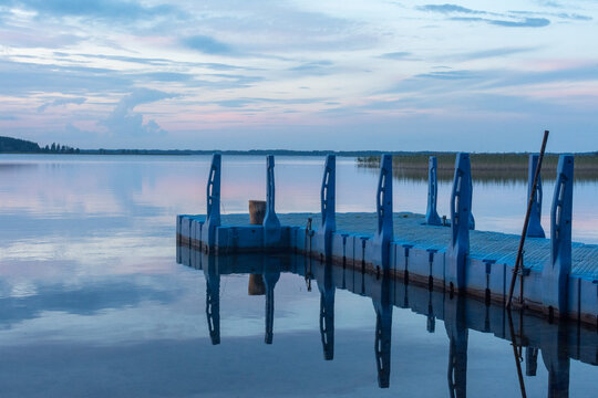 Blue plastic floating pier on a calm lake at sunset