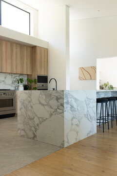 Marble waterfall island centering kitchen, featuring black faucet and sink, three black stools