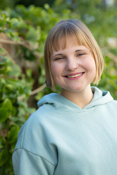 Female early twenties standing by green hedge, wearing blue hoodie and small nose ring