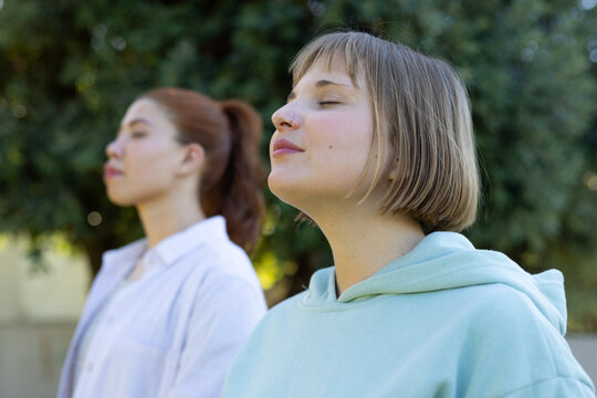 Female friends standing in garden, closing eyes, wearing blue hoodie, white shirt