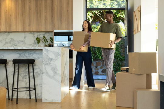 Couple carrying cardboard boxes walking through kitchen entry wearing olive tee and striped top