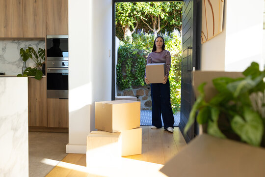 Asian woman holding cardboard box, wearing striped top and white sneakers in doorway