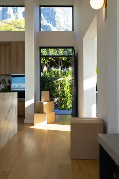 Stacked cardboard moving boxes are sitting near glass entry door, sunlight casting rectangles
