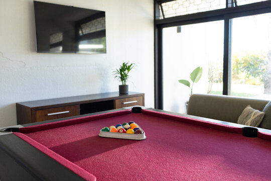 Red-felt pool table is featuring racked billiard balls in living game room with sunlight