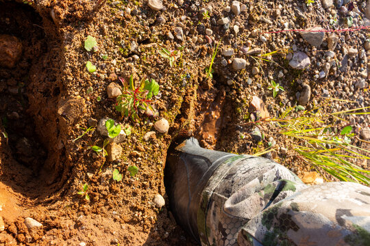 Rubber boot stuck in thick, deep mud on a countryside trail. A hiker wearing camouflage gear struggles while walking through a swampy, dirty, and wet outdoor landscape during autumn