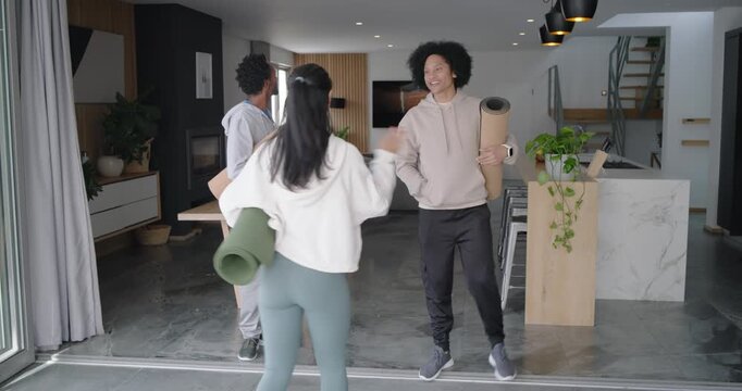 Three friends spotting tripod DSLR, walking at home wearing activewear, unrolling mats to record