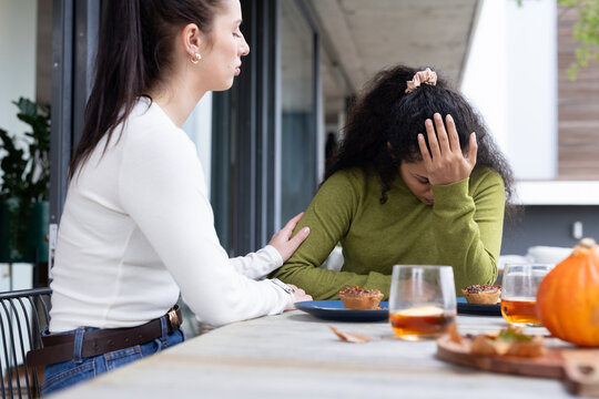 Two female friends comforting woman wearing green sweater on patio table with pastries, copy space