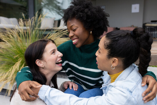 Diverse female friends sitting on porch steps with grasses, wearing denim and hoop earrings