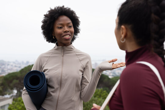 African American women standing at park overlook, wearing gray zip-up jacket and holding yoga mat