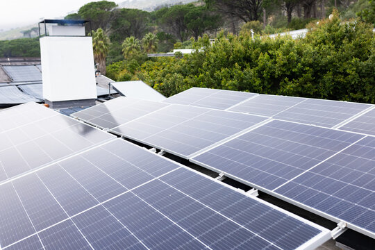Dark-blue solar panels are being mounted on rails on rooftop, with white chimney and misty treeline