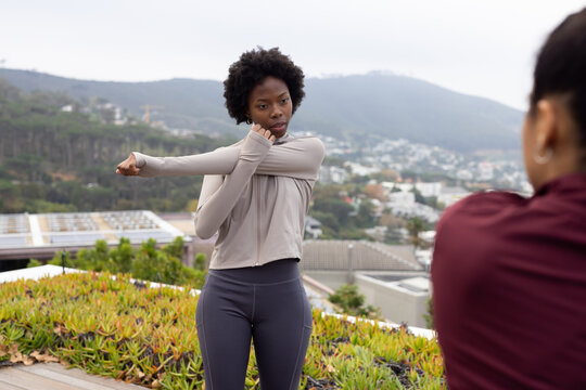 African women stretching and recording on rooftop with succulents and solar panels in athletic wear