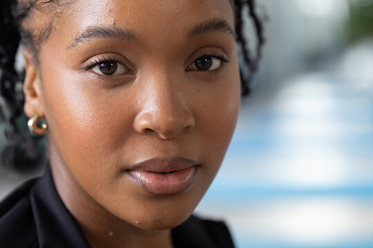 African woman looking at camera in outdoor portrait wearing dark blazer braided hair gold hoop