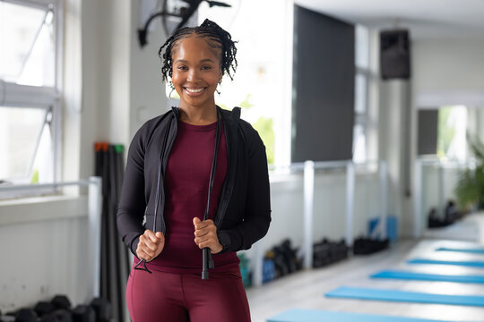 African American woman holding jump rope wearing maroon top with blue mats in fitness studio