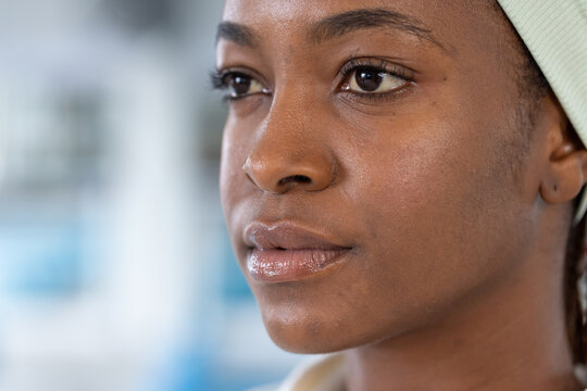 African adult female gazing toward camera, showing pale green headband and stud earring at pool