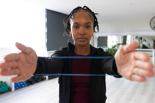 Adult African American woman wearing black zip-up jacket holding blue resistance band at gym