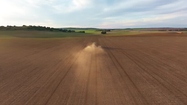 Rear view from drone perspective with tracking shot of a lone tractor working a field before the sowing season for future crops, with dust kicked up by the tractor as the soil is dry and dusty, Spain
