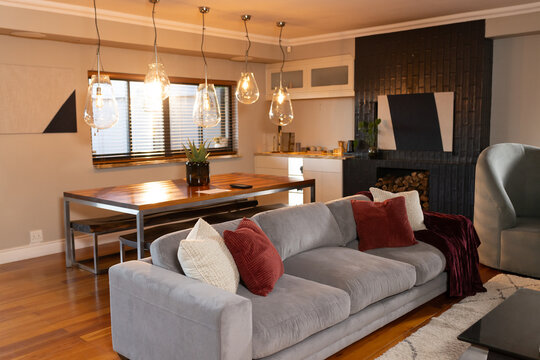 Light-gray sofa is positioned in warm living dining room with rust-red pillows and pendant lights