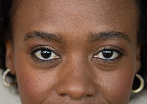 African American woman wearing gold-tone hoops, showcasing mascara and subtle eyeshadow in studio