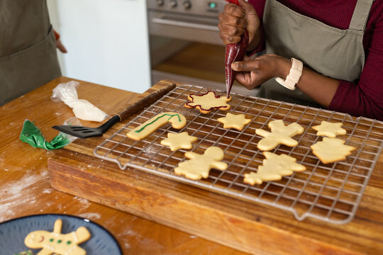 Baking partners with African baker in gray apron icing cookies on cooling rack using piping bags
