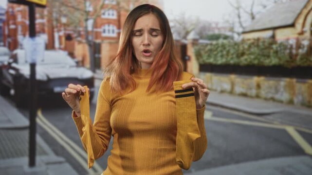 Woman holds yellow socks with both hands, pouting and showing a single sock on a street; disappointment inconvenience.