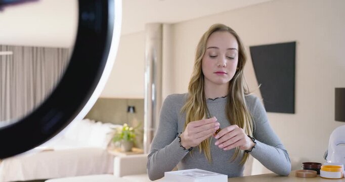 Woman arranging items, demonstrating skincare on camera using dropper and gua sha in bedroom