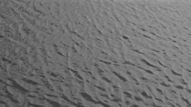 Monochrome water surface ripples in subtle slow motion. A close-up captures overlapping gray waves and flowing surface texture.